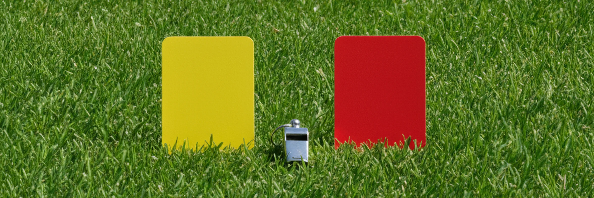 A referee's yellow card and red card on grass beside a whistle