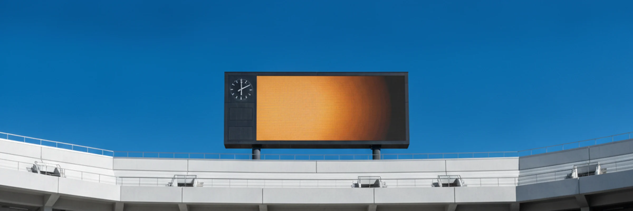 Stadium scoreboard and match clock against a blue sky